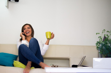 Hermosa mujer hablando por teléfono sentada en un sofá en la sala de su casa