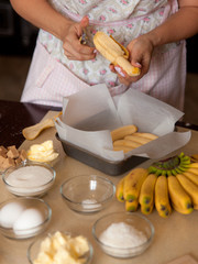 Female hands cut banans for the pie. Cooking process on kitchen. Ingredients for sweet fruit dessert on table.