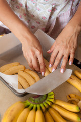 Female hands put banans in a baking dish. Cooking process on kitchen. Ingredients for sweet fruit dessert on table.