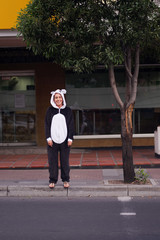 Close up of a happy woman wearing a panda costume, waiting in the sidewalk to cross the street, in the city of Quito