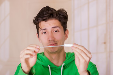 Handsome man with a funny face holding a menstruation cotton tampon in front of him, wearing a green hoodie in a blurred background