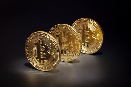 macro three golden bitcoins in a row on black background. virtual cryptocurrency concept