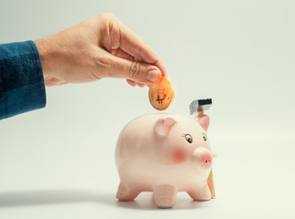 male hand putting bitcoin in to piggy bank. cryptocurrency investment concept