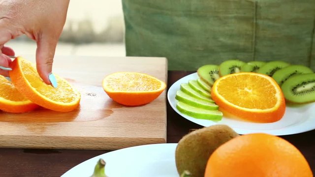 Vegetarian diet. A woman puts pieces of orange on a plate, which is on a cutting board. Full Hd shot with dolly from left to right.