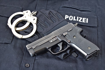 Pistole mit Handschellen und Handschuhen auf Uniformhemd mit dem Aufdruck "Polizei"