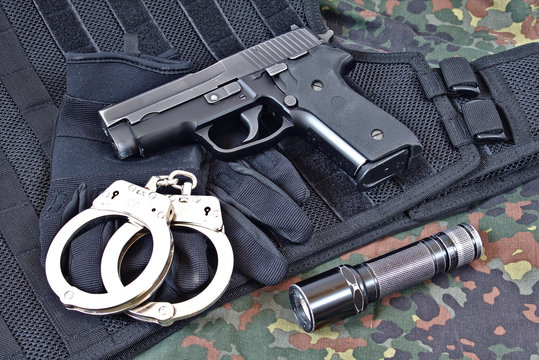 Handgun with handcuffs, gloves and flashlight on tactical vest and camouflage clothing