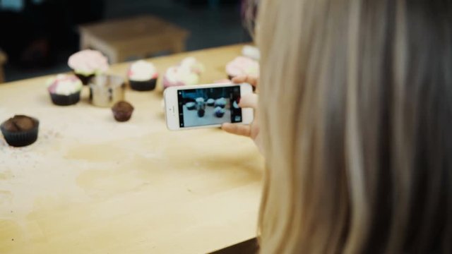 Close-up view of female taking photos of cupcakes with she has baked. Young woman using the camera on smartphone.