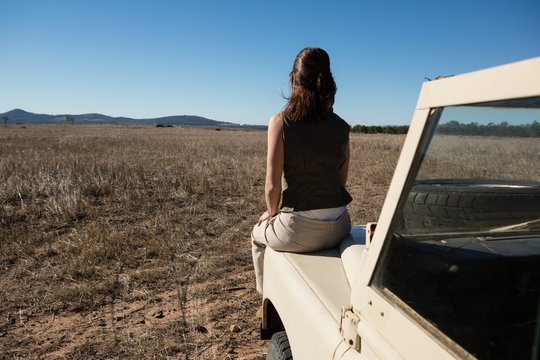 Rear view of woman on vehicle hood at landscape