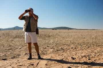 Man looking through binocular while standing on landscape