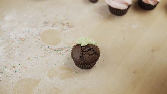 Close-up view of female hands decorating the chocolate cupcake with colored cream, using pastry bag for this.