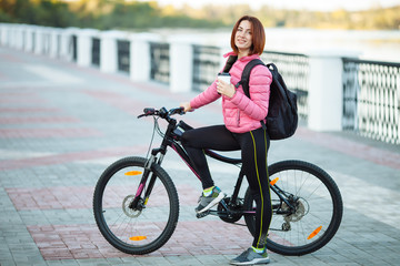 Obraz na płótnie Canvas Adult beautiful redhead woman with bob haircut thinking drinking morning coffee posing on bicycle in autumn city river pier