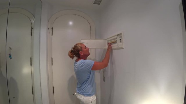 Woman checking and turning on circuit breakers in electrical fuse box at her house