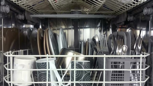 Elevating shot of the inside of a dish washer loaded with crockery and cutlery after a wash