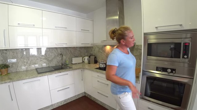 Woman in kitchen using microwave oven looking at the camera and smiling
