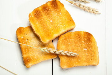 Toasts and wheat on a white wooden background