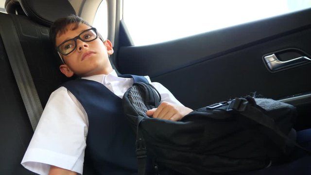 the sad boy is riding in the car in school uniform. 4k, slow-motion