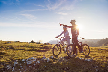 Biker couple with mountain bike pointing in distance at countryside - Powered by Adobe