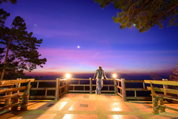 Hipster male backpacker standing and relaxing at mountain view point with star and twilight sky in the evening.