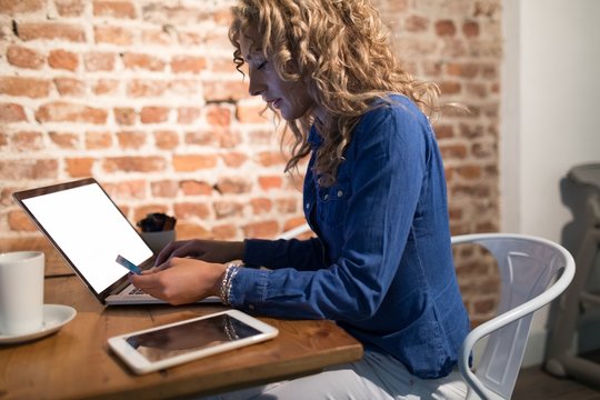 Side view of woman holding credit card while using laptop
