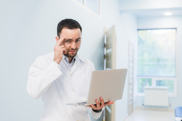 Fototapeta premium Portrait of cheerful doctor sitting at the desk working on laptop