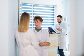 Mature doctor discussing with nurses in a hallway hospital. Doctor discussing patient case status with his medical staff after operation.