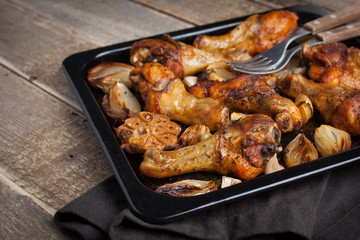 Oven-baked chicken leg quarters with onion, garlic and capsicum on a dark background closeup