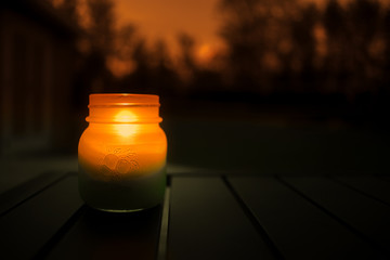 A close up of a lit candle in a mason jar outdoors in the evening