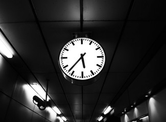 The clock at the railway station show the time while people waiting train to working office white black white.