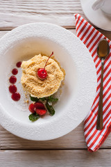 Napoleon cake on white plate with decoration from strawberry, cherry and mint. Sweet dessert serving in restaurant on wooden table, close up top view