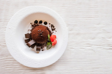 Chocolate fondant with decoration from strawberry and mint on wooden table. Delicious dessert serving in restaurant, top view with free space