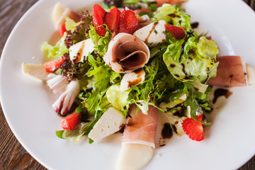 Salad lettuce with parma ham, blue cheese and strawberry serving in restaurant on wooden table. Gourmet cuisine close up picture