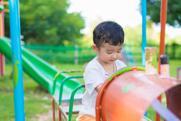 Young Asian boy play a iron train swinging at the playground under the sunlight in summer.