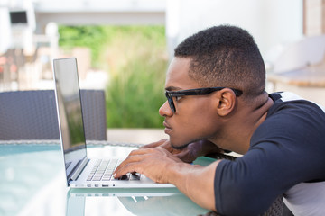 Closeup portrait, young nerdy man in big black glasses surfing the web on personal silver laptop,...