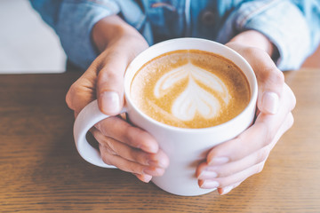 Woman's hand holding a coffee latte cup art on wooden desk