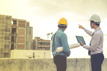 smiling young architect or engineering builder in hard hat with tablet over group of builders at...