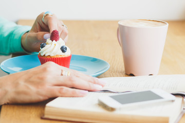 Cup with cappuccino, cupcake on the plate and a book with a phone