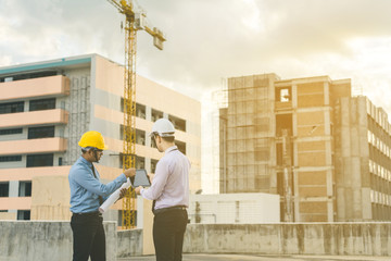 smiling young architect or engineering builder in hard hat with tablet over group of builders at...