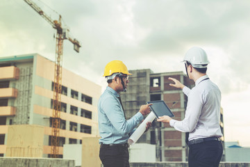 smiling young architect or engineering builder in hard hat with tablet over group of builders at...