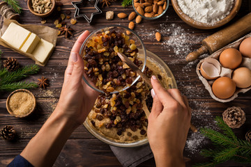 young woman's hands cooking christmas fruit cake. Wooden table with baking ingredients.