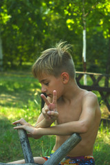  portrait. boy. blond. on a wooden swing. looks down. shows the sign of viktori