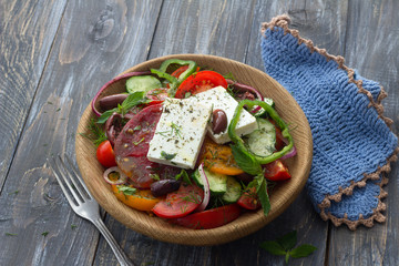 Homemade Greek salad from tomatoes, cucumbers, sweet peppers, cheese, olives and greens in a wooden bowl on a wooden table with free space. Healthy delicious food