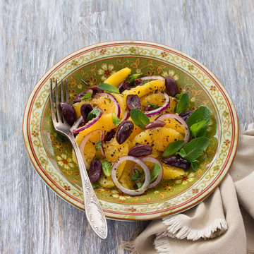Moroccan salad of oranges with red onions, olives and zira on a wooden table