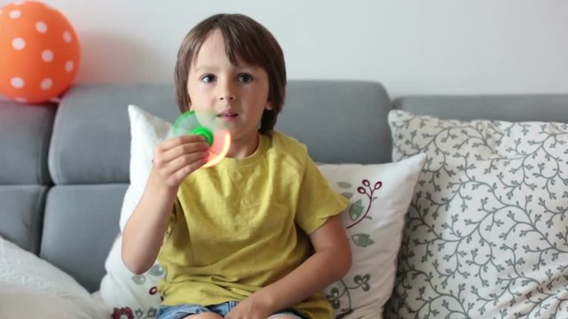 Little child, boy, playing with green and blue luminous fidget spinner toy to relieve stress at home