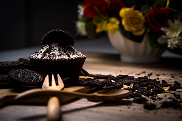 Homemade dark chocolate cupcake with chocolate cookies on the wood table and flower background, selective focus