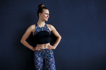 Fototapeta na wymiar Beautiful fitness model is posing in front of the dark wall in a dark training suit
