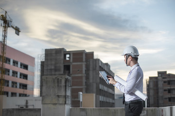 Smiling young architect or engineering builder in hard hat with tablet over group of builders at construction site, architect watching some a construction, business, building, industry, people concept