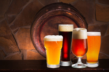 Set of various glasses of beer in cellar, pub or restaurant. Beer glasses, old beer barrel and brick wall on background. Still life with ale