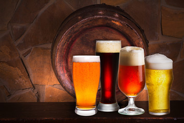 Set of various glasses of beer in cellar, pub or restaurant. Beer glasses, old beer barrel and brick wall on background. Still life with ale