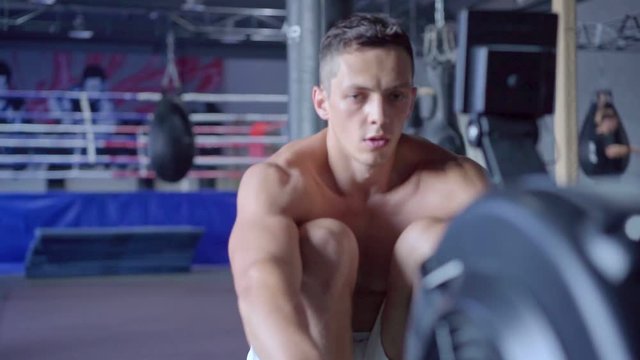 Young athletic man doing rowing machine workout at the gym