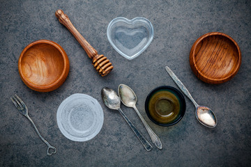 Various cooking utensils border. Wooden bowl , vintage spoons and honey dipper on dark stone background with flat lay .
